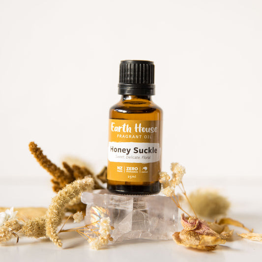 A bottle of 'Honey Suckle' fragrance oil from Earth House, surrounded by dried flowers and crystal stones.