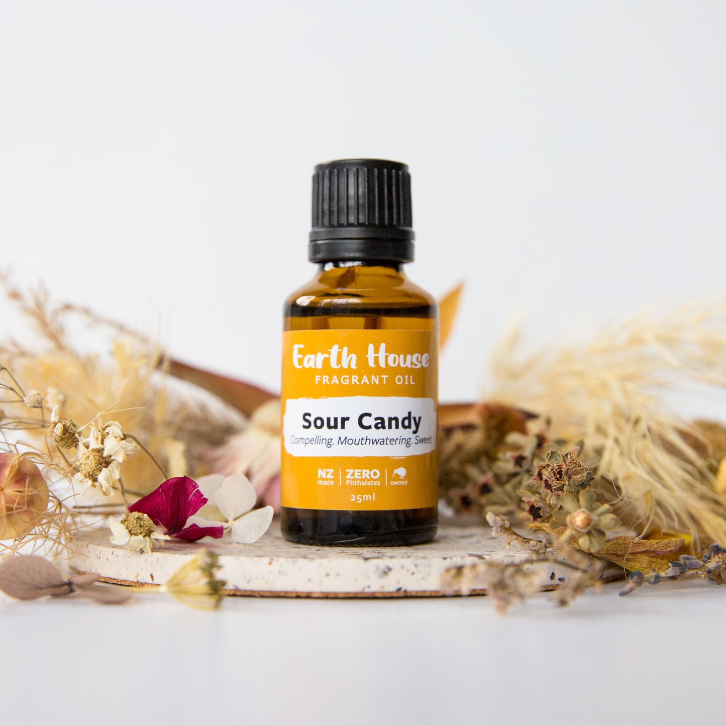 Bottle of Sour Candy fragrant oil from Earth House surrounded by dried flowers on a white background
